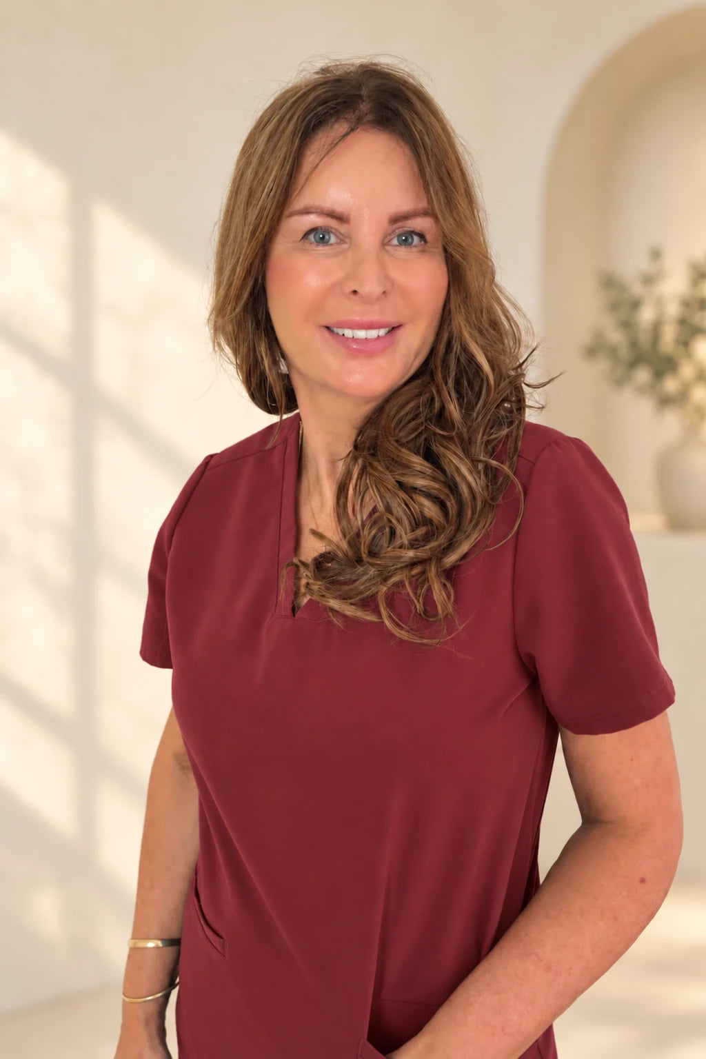 Debbie Lamkin in burgundy nursing scrubs, with an edited background